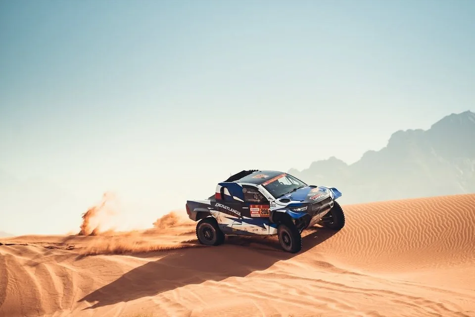 Auto des Energylandia Rally Team auf einer Düne vor den Bergen Saudi-Arabiens