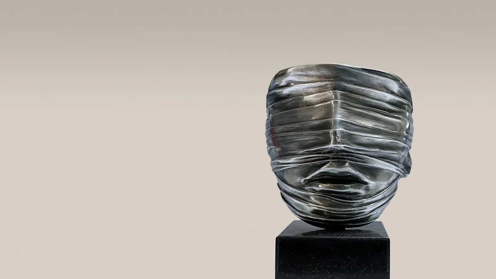 Igor Mitoraj, »Tilsløret ansigt«, 1977 – sølvskinnende skulptur af et ansigt svøbt i bånd, på sort sokkel