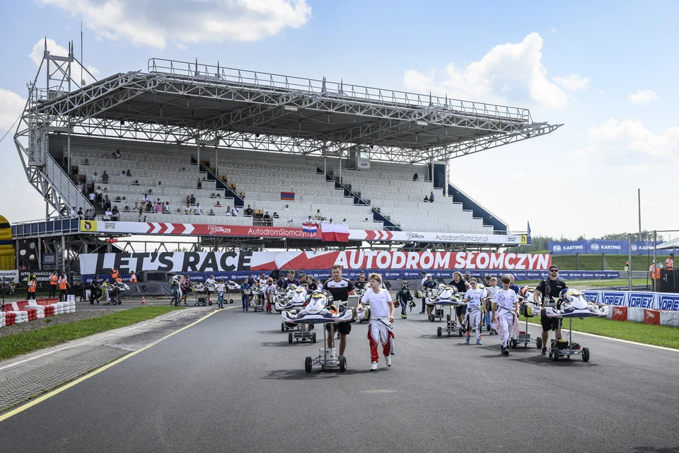 Mechanicy wyprowadzają gokarty na wózkach przed trybuną główną Autodromu Słomczyn