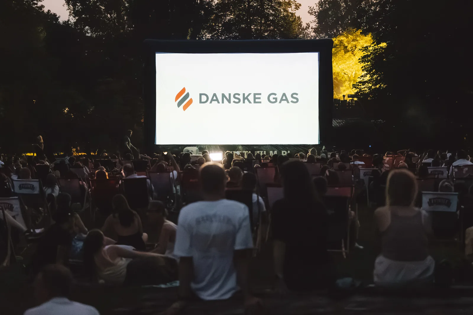 Sommerbiografens lærred på Pole Mokotowskie med Danske Gas’ logo, publikum i liggestole i tusmørket