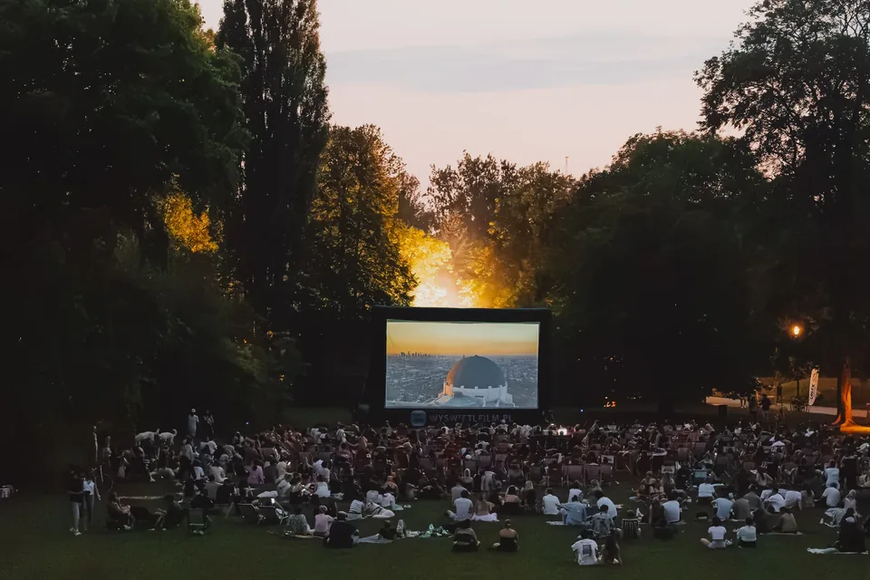 Lichtung des Sommerkinos LOLEK in der Abenddämmerung – Leinwand zwischen Bäumen und Zuschauer im Gras
