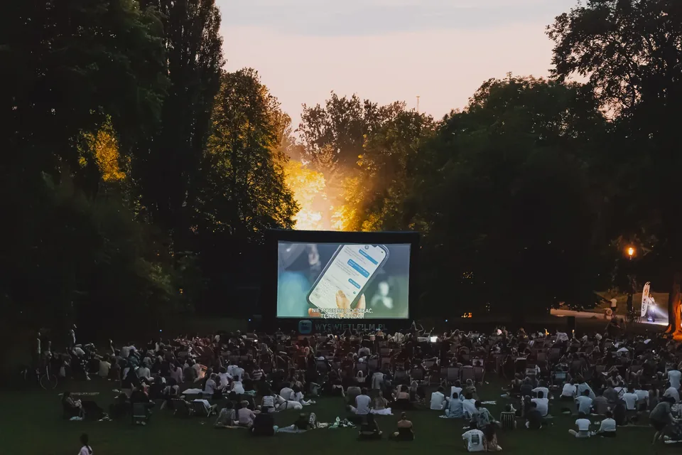 Zuschauer des Sommerkinos im Gras, die Leinwand nach Einbruch der Dunkelheit erleuchtet